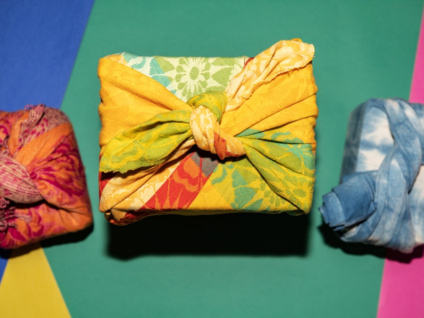 Photograph of three gifts wrapped in fabric photographed from overhead against a colorful background.