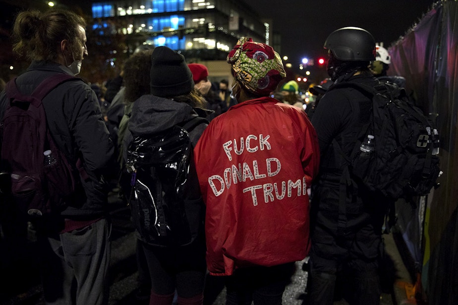 caption: Protester Angelica C. wears a jacket that reads 'Fuck Donald Trump,' while marching through the South Lake Union neighborhood with multiple groups protesting for racial justice and against police brutality on the night of the 2020 presidential election, on Tuesday, November 3, 2020, in Seattle.