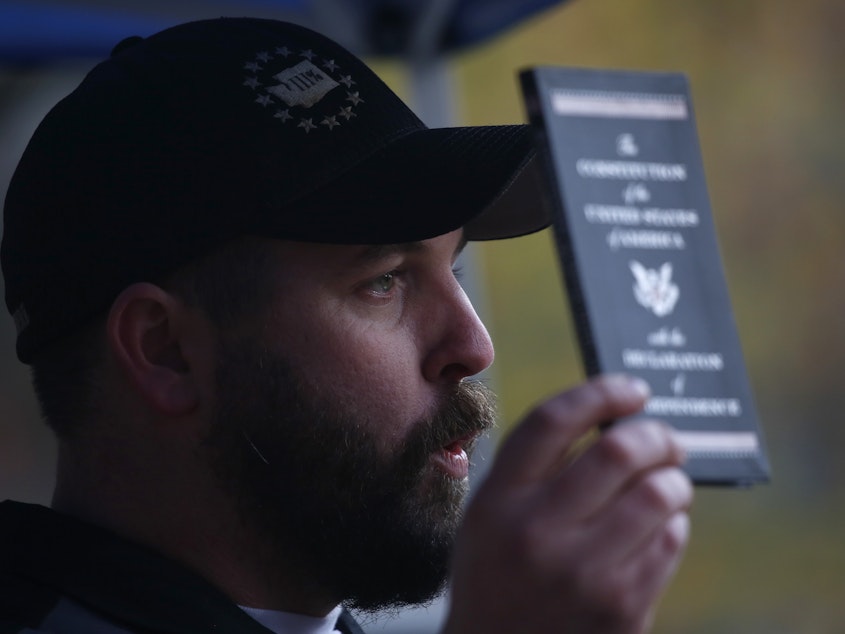 caption: Matt Marshall, state leader of the Washington Three Percent, holds the U.S. Constitution during the "United Against Hate" rally.