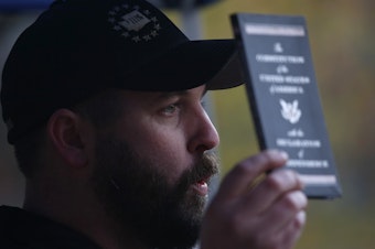 caption: Matt Marshall, state leader of the Washington Three Percent, holds the U.S. Constitution during the "United Against Hate" rally.