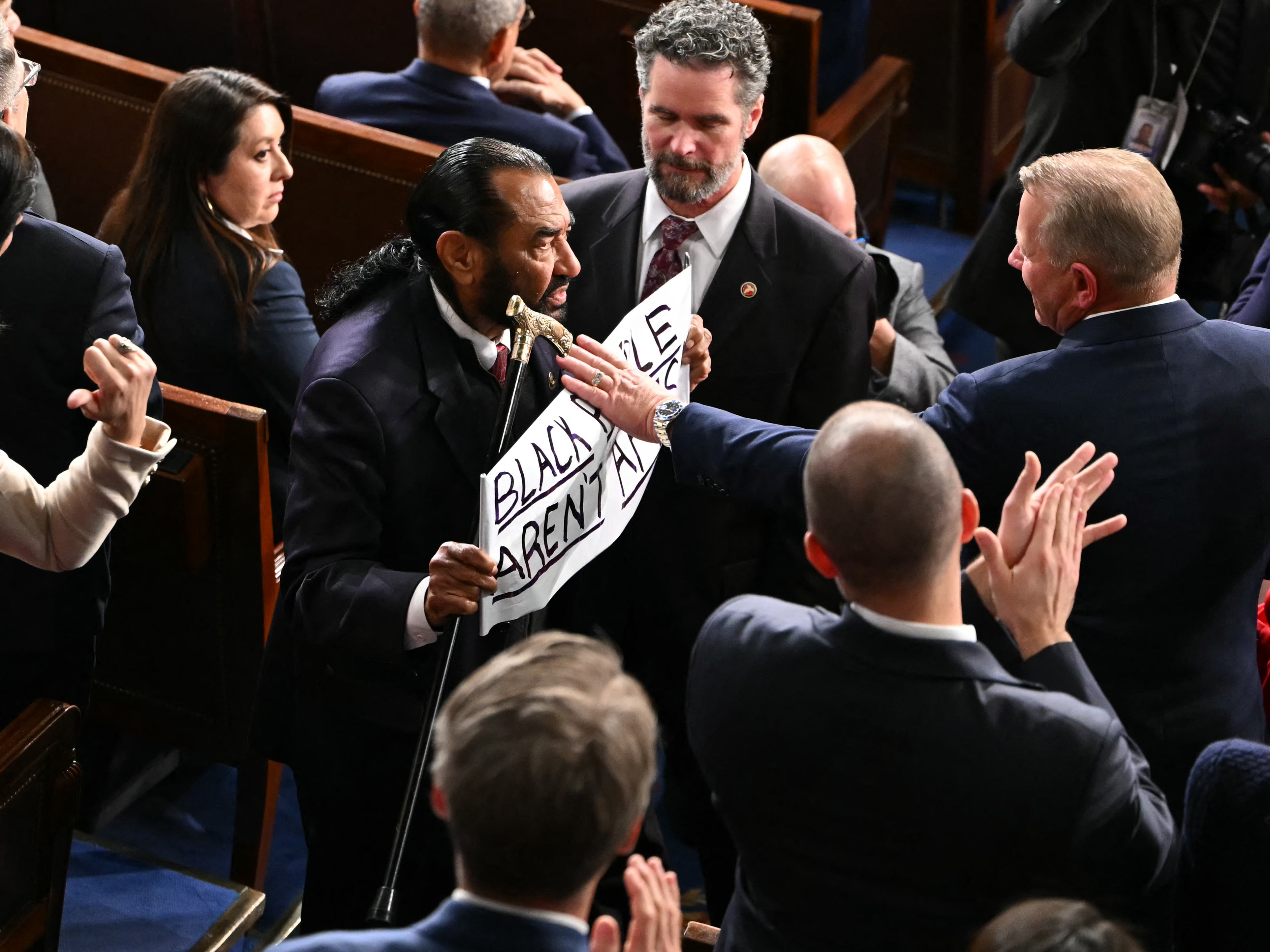 caption: U.S. Rep. Al Green, D-Texas, exits as he holds a sign reading "Black people aren't apes" during President Trump's State of the Union address in the House Chamber of the U.S. Capitol in Washington, D.C., on Tuesday.