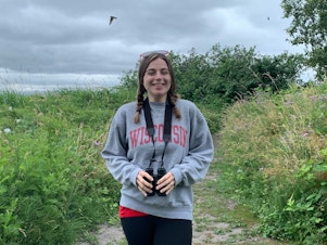 caption: Birder and Ph.D. candidate in avian research Olivia Sanderfoot poses near the Center for Urban Horticulture in Seattle, while swallows swoop in the background.