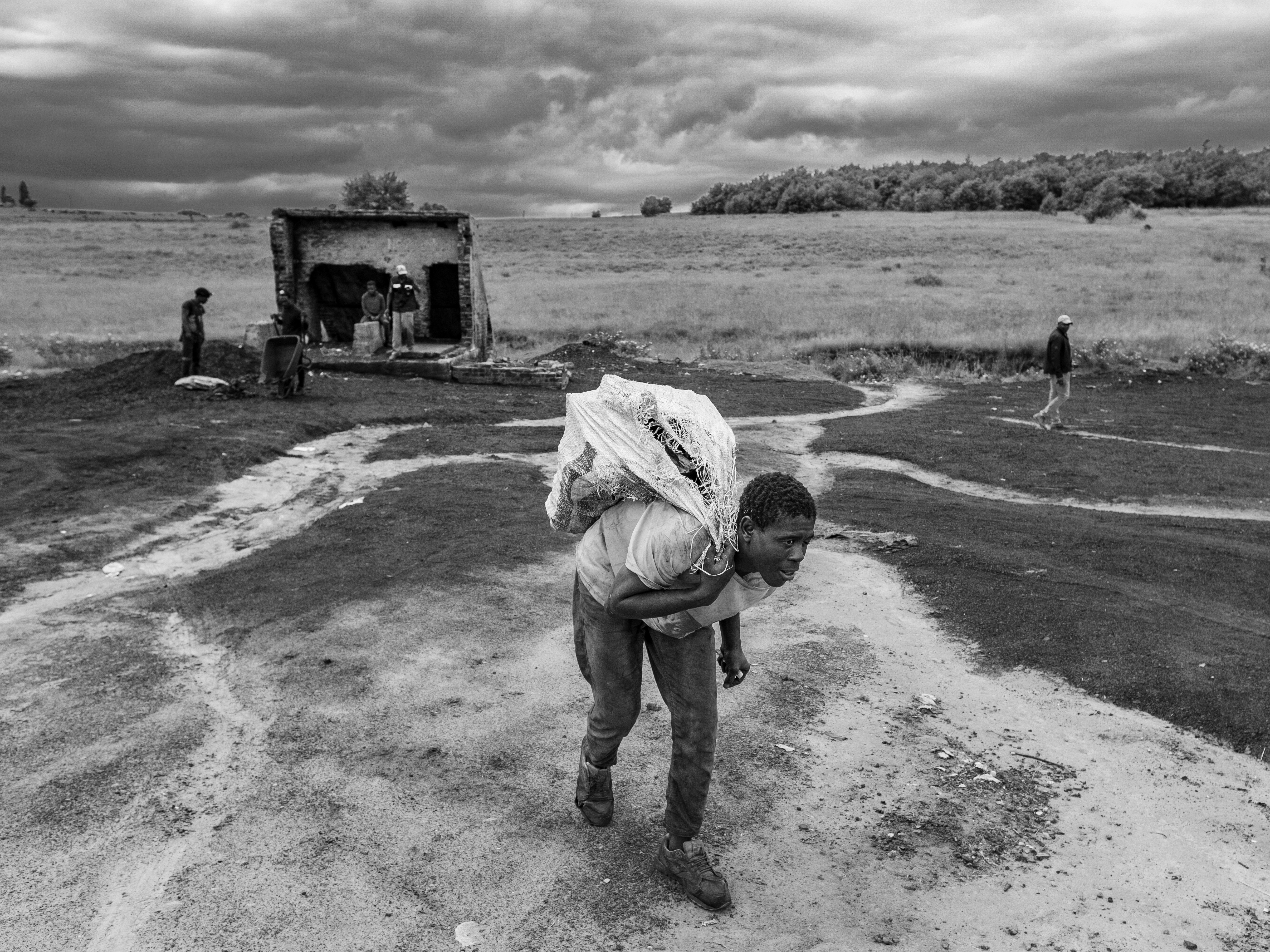 caption: Artisanal coal miner Emmanuel Siyabonga hauls a sack of coal to a client's car at the abandoned Golfview coal mine in Ermelo, South Africa. The work is grueling and hazardous but is one of the few viable means of making a living in a town with widespread poverty and high rates of unemployment.