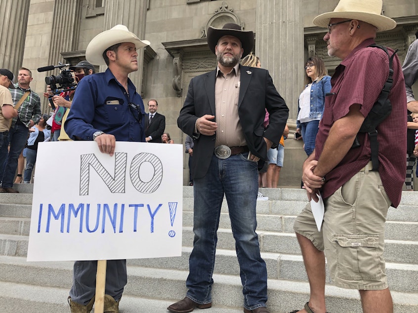 caption: Ammon Bundy, center, who led a protest at a Boise hospital last year, stands on the Idaho Statehouse steps in Boise, Idaho, on Monday, Aug. 24, 2020.