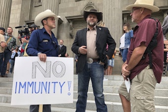 caption: Ammon Bundy, center, who led a protest at a Boise hospital last year, stands on the Idaho Statehouse steps in Boise, Idaho, on Monday, Aug. 24, 2020.
