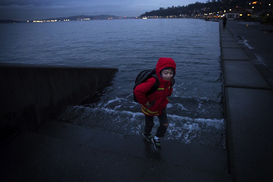 caption: Ely Thomas, 7, runs from water spilling over a set of stairs  during a King Tide at Alki Beach Park on Friday, January 5, 2018, in West Seattle. 