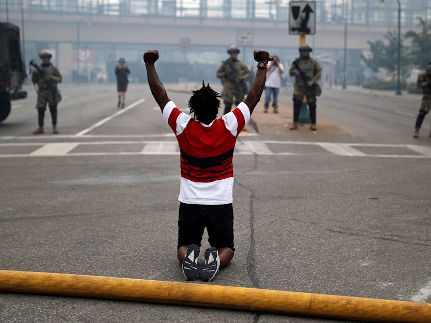 caption: A man kneels as he confronts National Guard members guarding the area in the aftermath of a protest in Minneapolis, Minn.