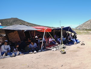 caption: A group of people wait to be processed after crossing the border between Mexico and the United States as they seek asylum in April 2024, near Jacumba, Calif.