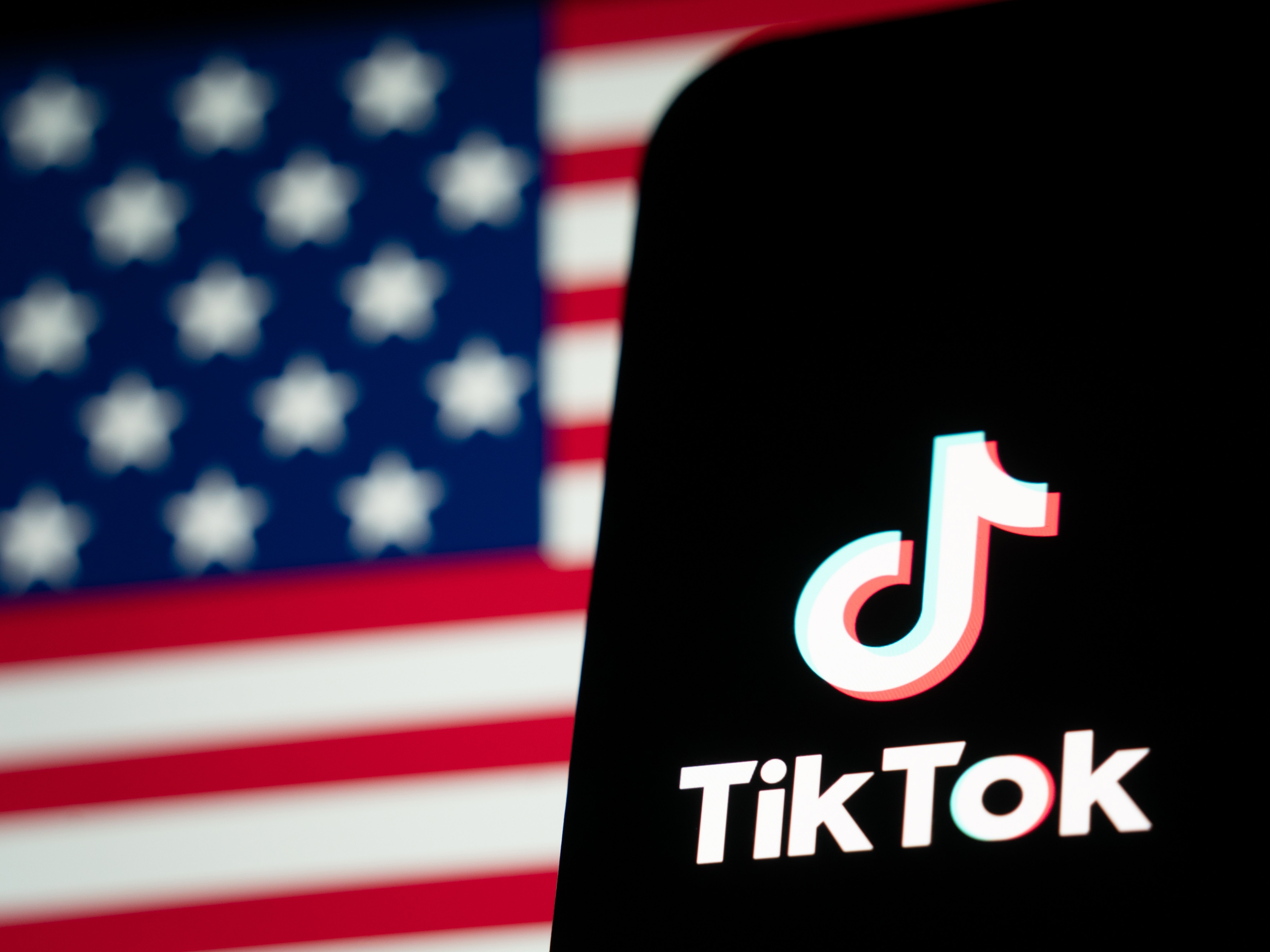 caption: In this photo illustration, the TikTok logo and flag of the United States are seen on screens in January 2025 in Hong Kong.