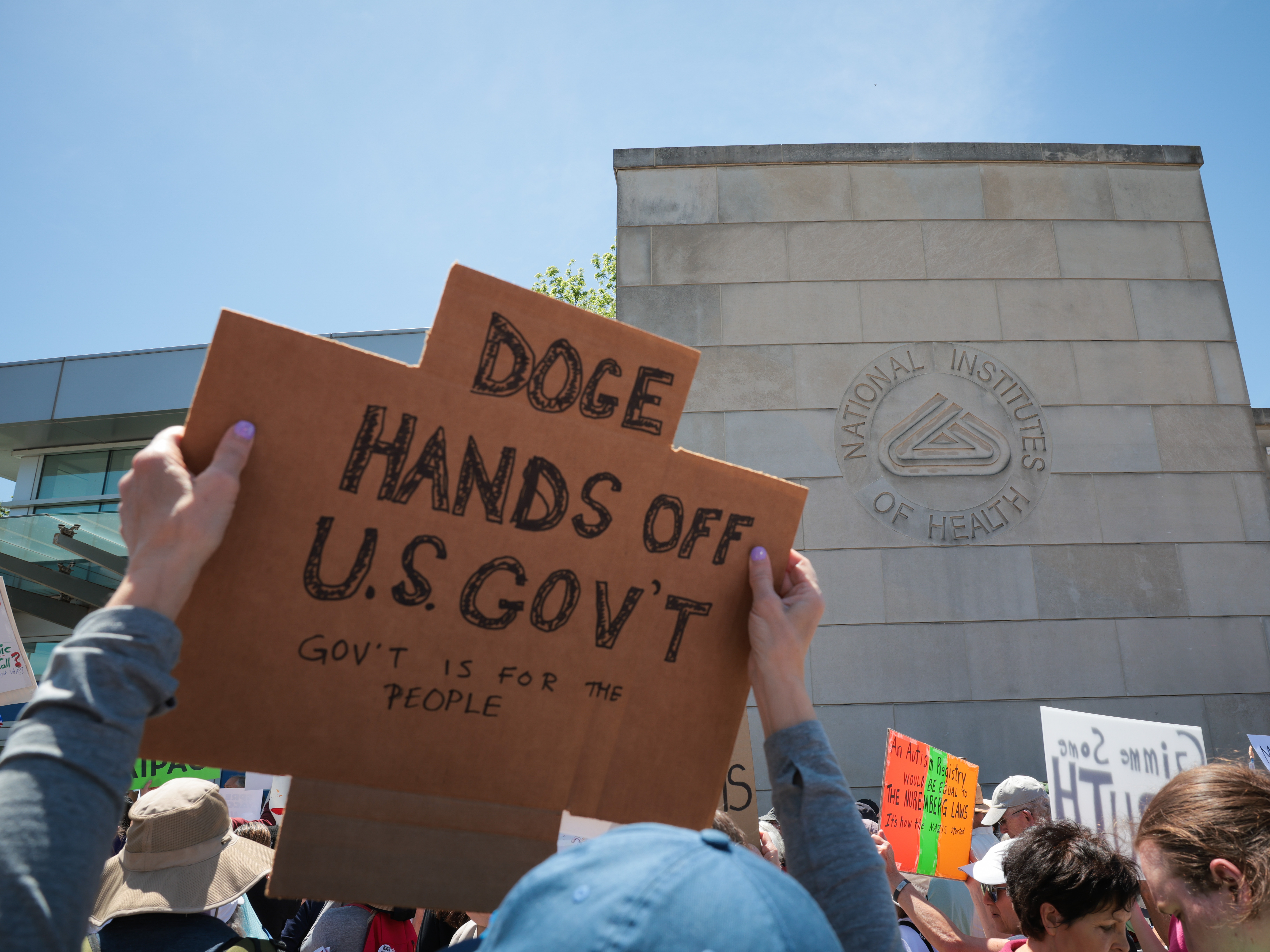 caption: Demonstrators raise signs during a rally outside the National Institutes of Health on May 10 in Bethesda, Md.