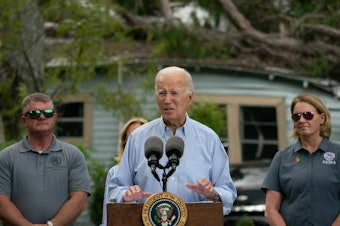caption: President Biden speaks in front of a home destroyed by fallen trees and debris during a tour of communities impacted by Hurricane Idalia, in Live Oak, Fla., on Saturday.