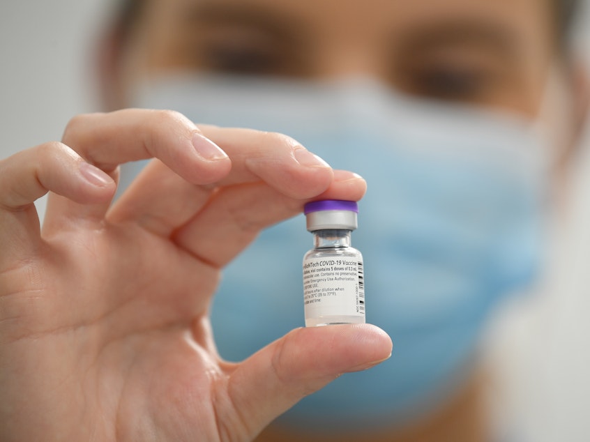 caption: A staff member poses with a vial of Pfizer-BioNTech COVID-19 vaccine at a vaccination health center.