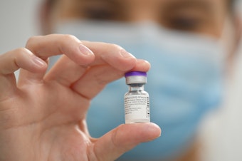 caption: A staff member poses with a vial of Pfizer-BioNTech COVID-19 vaccine at a vaccination health center.