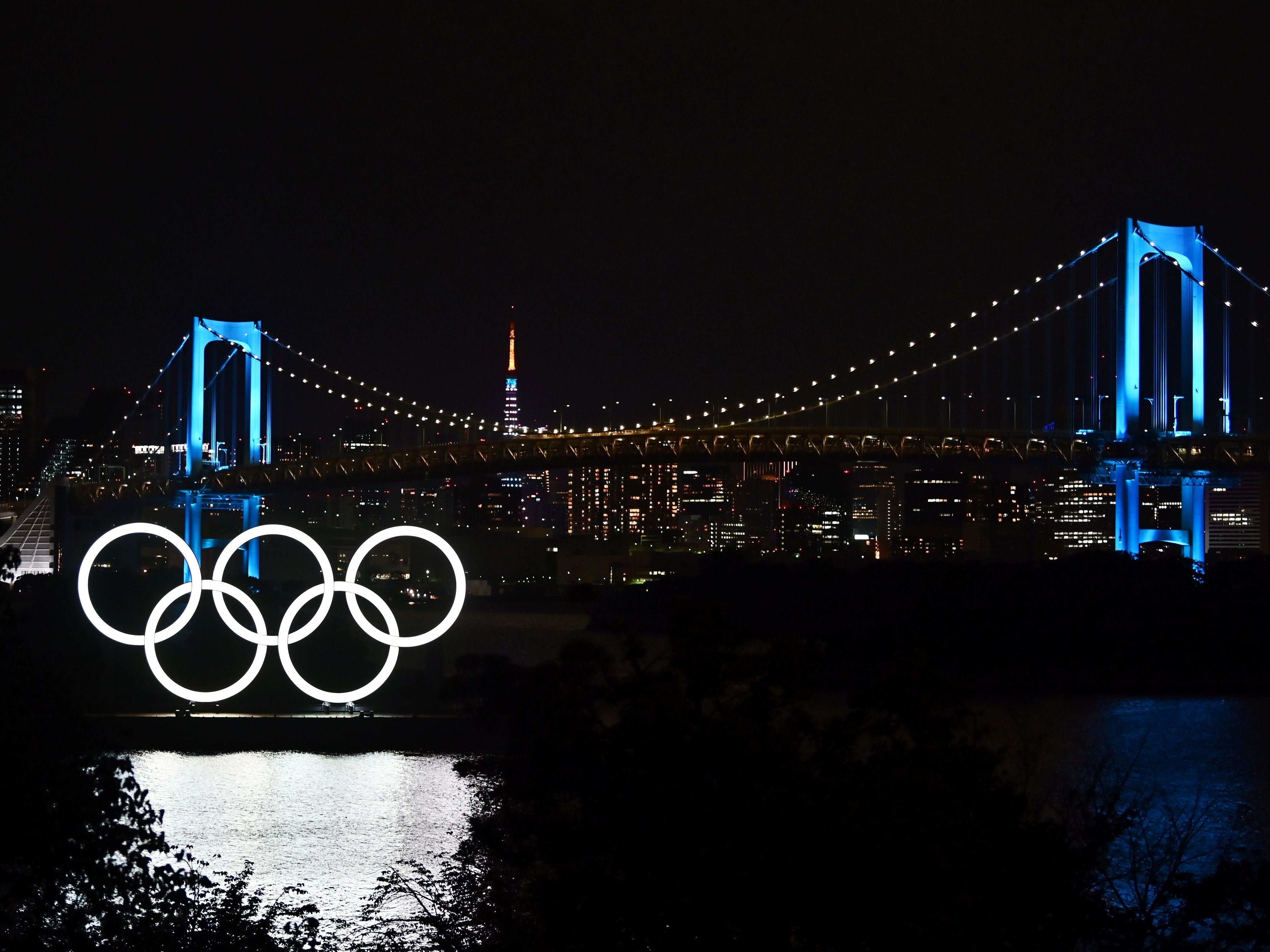 caption: "We shall all need to make sacrifices and compromises" to put on the Tokyo 2020 Olympics, IOC President Thomas Bach says, announcing funding to help keep the delayed games on track. The Olympic rings, the Rainbow Bridge and the Tokyo Tower are seen in Tokyo Friday night.