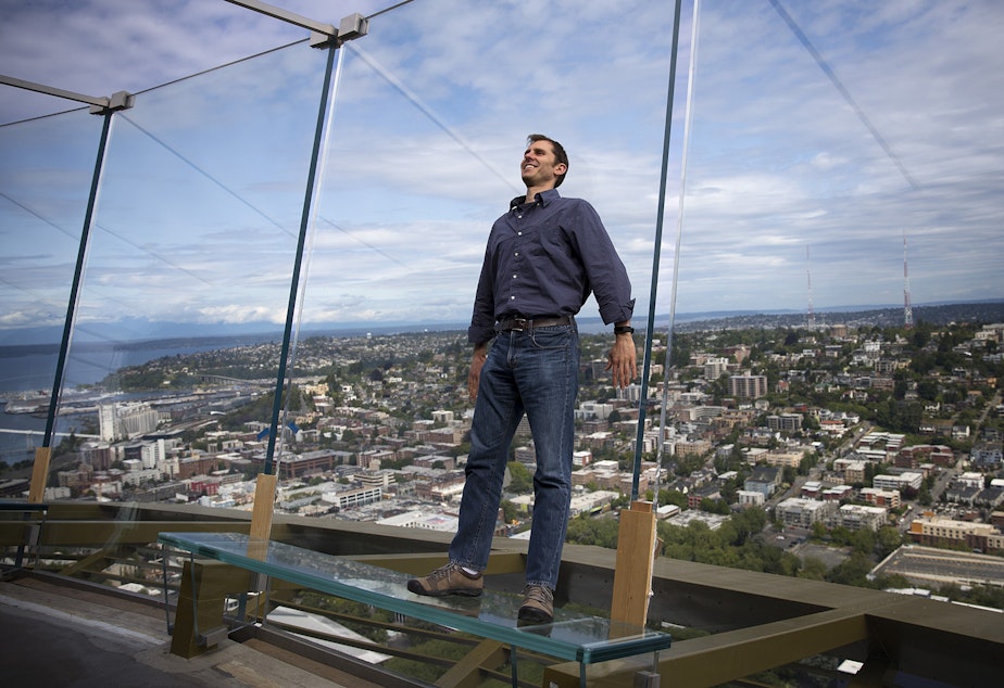 caption: Derek Hanson stands on a glass bench on the observation deck of the Space Needle on Tuesday, June 5, 2018, in Seattle. Hanson asked KUOW what would happen to the Space Needle in the event of an earthquake.