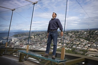 caption: Derek Hanson stands on a glass bench on the observation deck of the Space Needle on Tuesday, June 5, 2018, in Seattle. Hanson asked KUOW what would happen to the Space Needle in the event of an earthquake. 