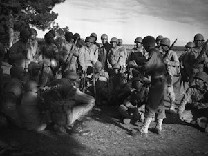 caption: Lt. Frank J. Crawford of Detroit, Michigan, as the Regimental plans and training officer, is giving his men instructions in combat maneuvers.