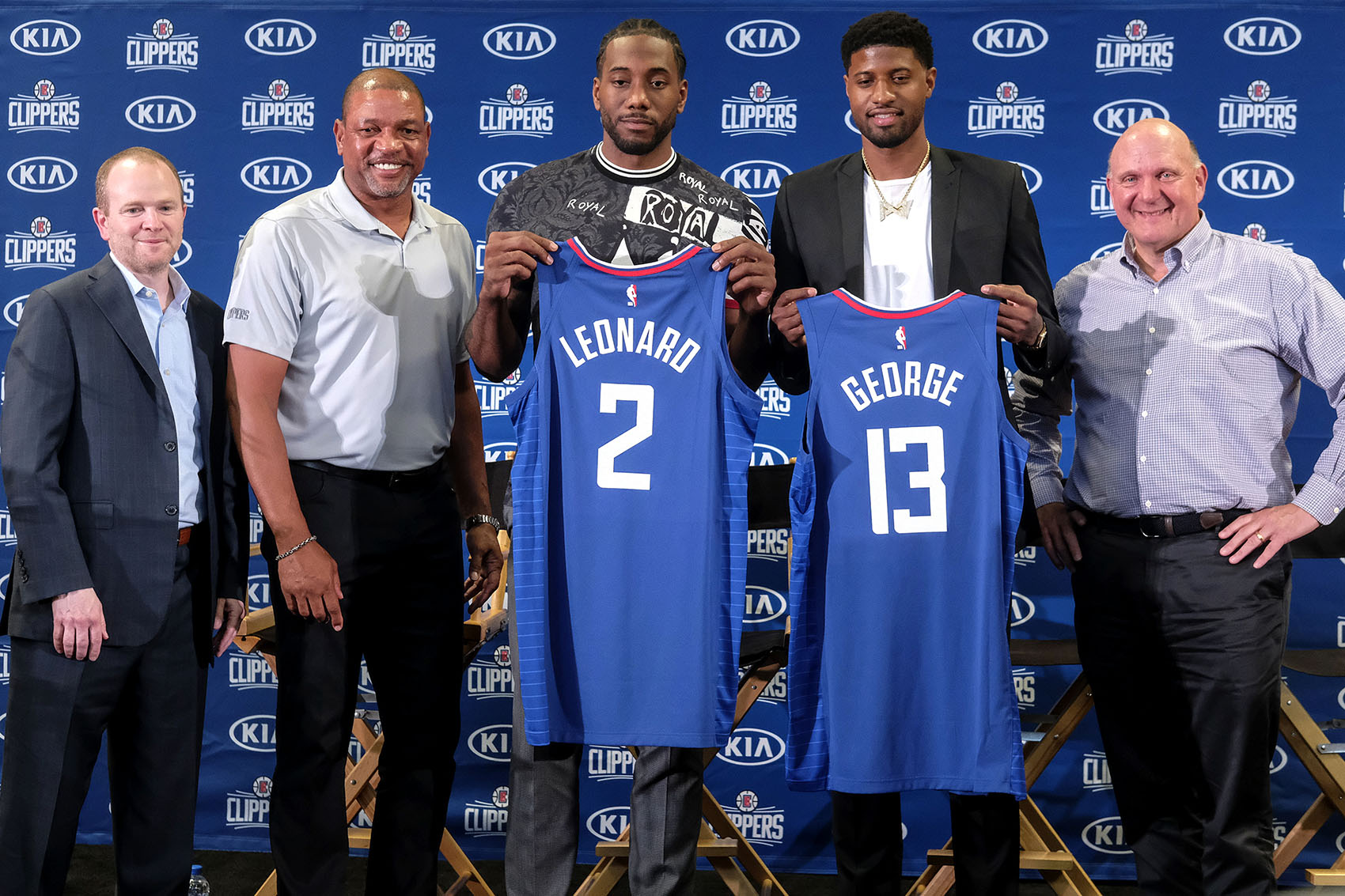 caption: Kawhi Leonard, center, and Paul George, second from the right, holding their new team jerseys, pose with Los Angeles Clippers President of Basketball Operations Lawrence Frank, left, head coach Doc Rivers, second from the left, and team chairman Steve Ballmer during a press conference in Los Angeles, Wednesday, July 24, 2019. (Ringo H.W. Chiu/AP)