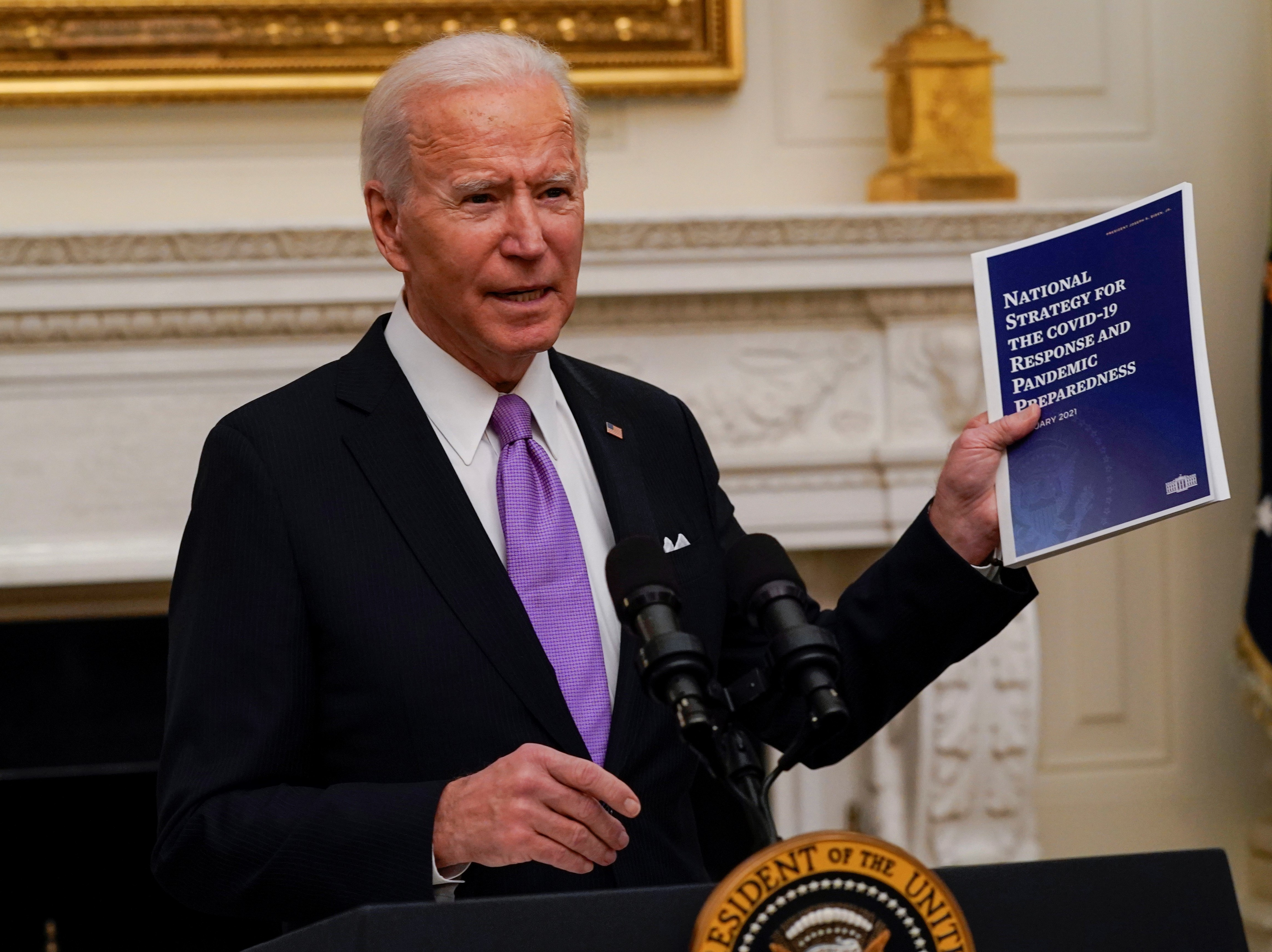 caption: President Joe Biden holds a booklet as he speaks about the coronavirus in the State Dinning Room of the White House, Thursday.