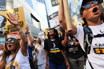 caption: People hold signs as members of SAG-AFTRA and Writers Guild of America East walk a picket line outside of the HBO/Amazon offices during the National Union Solidarity Day in New York City on Aug. 22, 2023. Labor unions have notched some big victories this year but organized labor still faces an uncertain future.