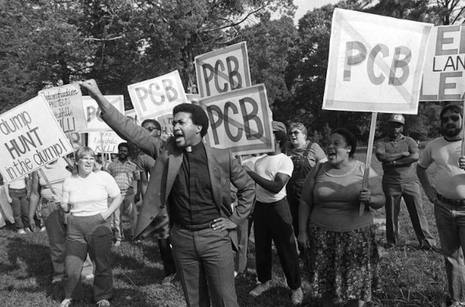 caption: Rev. Ben Chavis, right, raises his fist as fellow protesters are taken to jail at the Warren County PCB landfill near Afton, N.C., on Sept. 16, 1982.