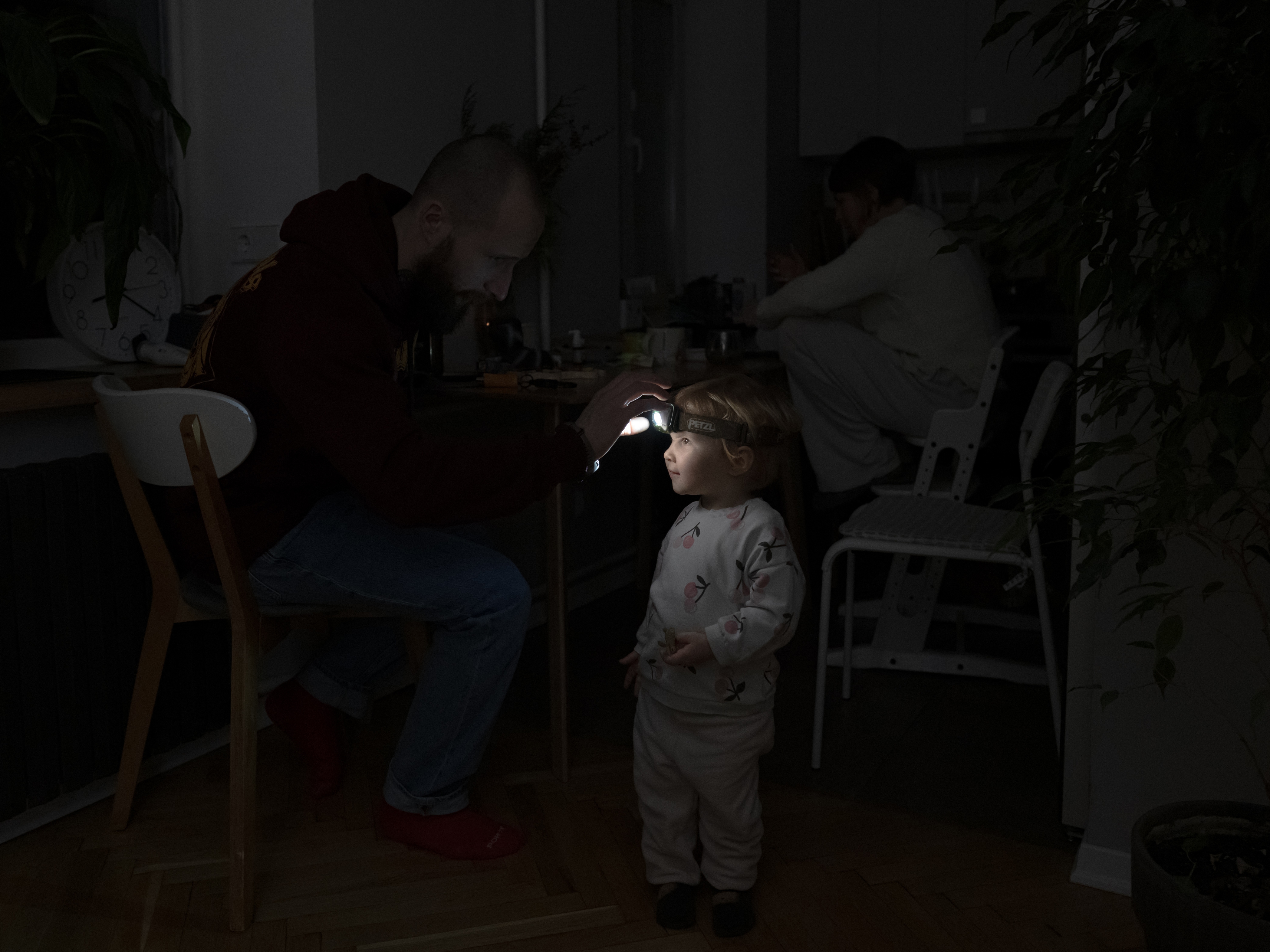 caption: A resident in Kyiv, Ukraine, helps his 2-year-old daughter use a headlight during a power outage at their apartment amid the Russian invasion of Ukraine.