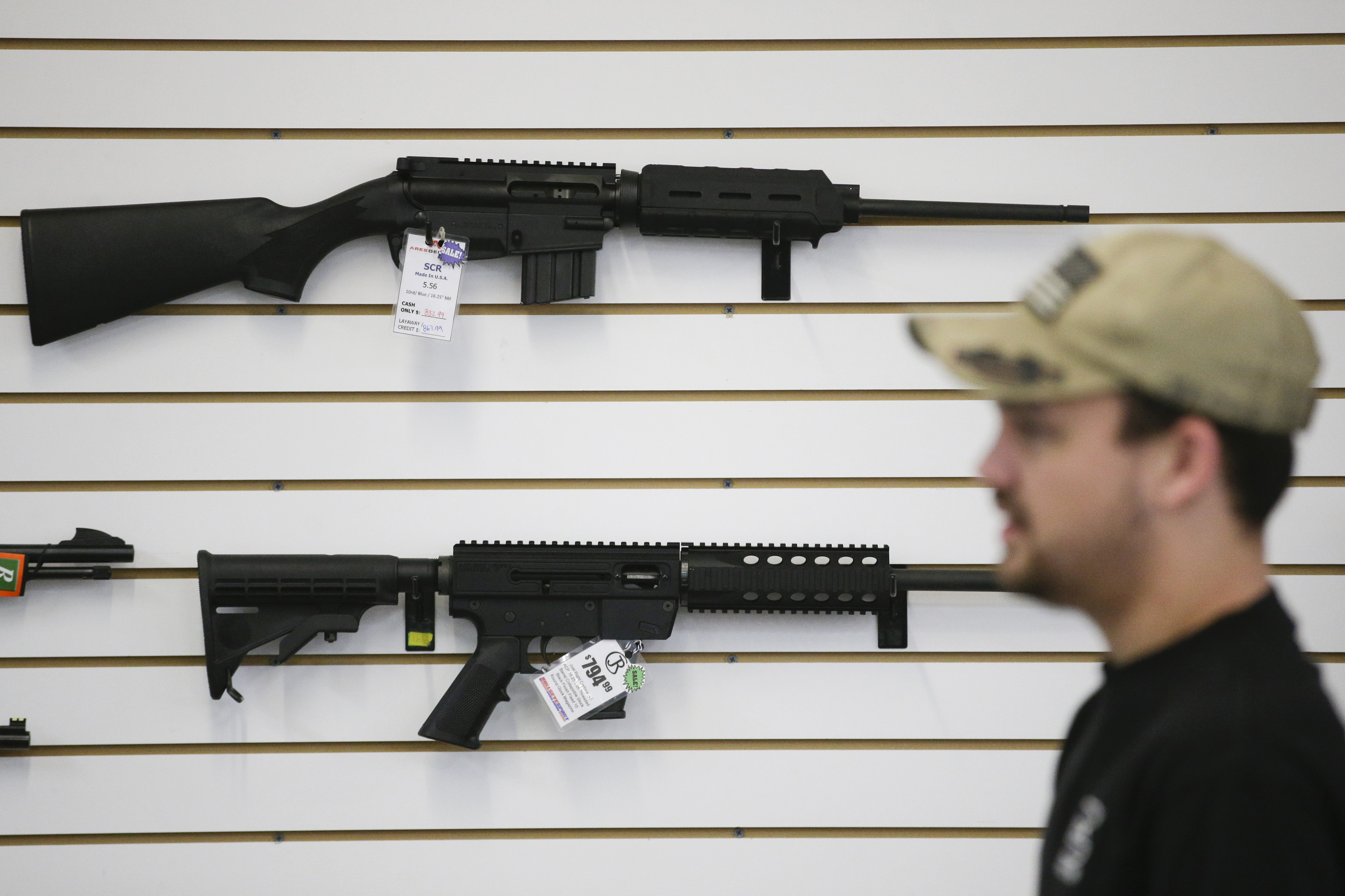caption: In this Dec. 9, 2015, photo, a sales associate walks past semiautomatic rifles at Bullseye Sport gun shop in Riverside, Calif.