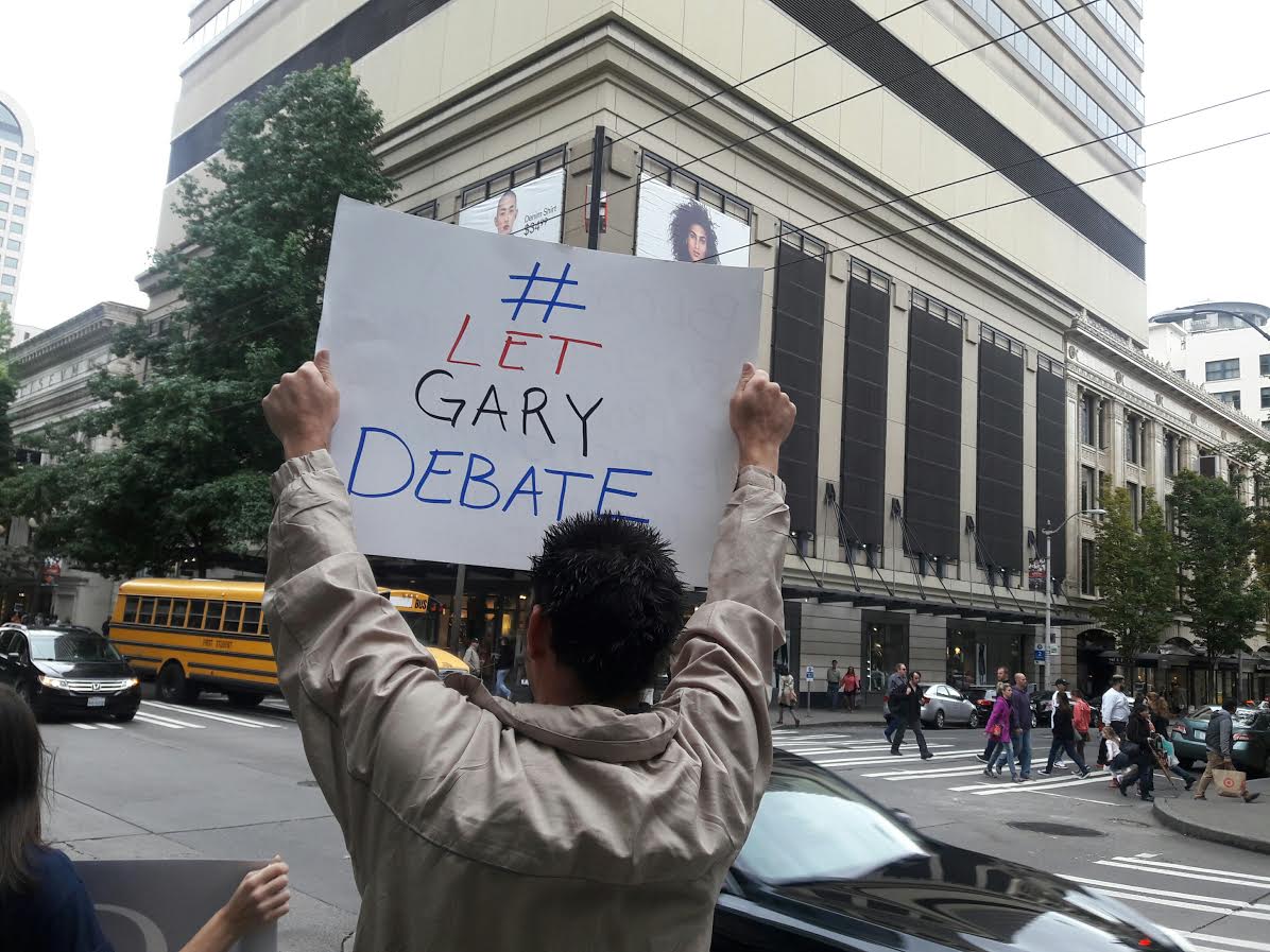 caption: Trifin Sergieff of Des Moines, Washington, held the sign. He says Johnson's message in debate would be less war, and lower taxes.