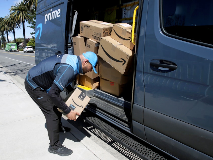 caption: A driver picks up a package while making deliveries for Amazon in Costa Mesa, Calif., on March 23. Amazon is offering to permanent jobs for 125,000 workers it hired to deal with a sharp rise in online shopping during the coronavirus pandemic.
