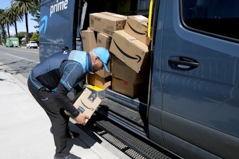 caption: A driver picks up a package while making deliveries for Amazon in Costa Mesa, Calif., on March 23. Amazon is offering to permanent jobs for 125,000 workers it hired to deal with a sharp rise in online shopping during the coronavirus pandemic.