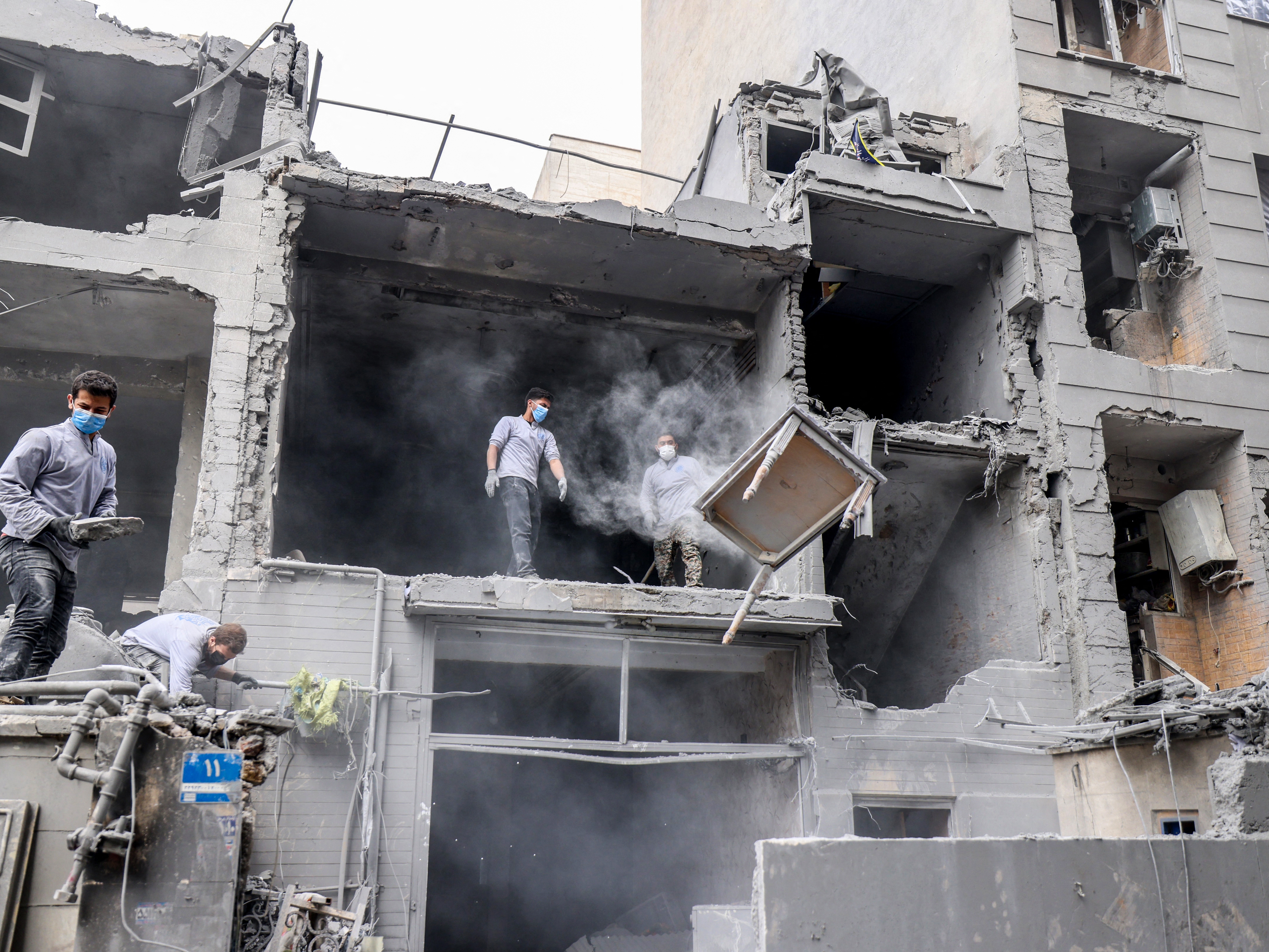 caption: Iranians clear the debris from damaged homes following a military strike in Tehran on March 15.