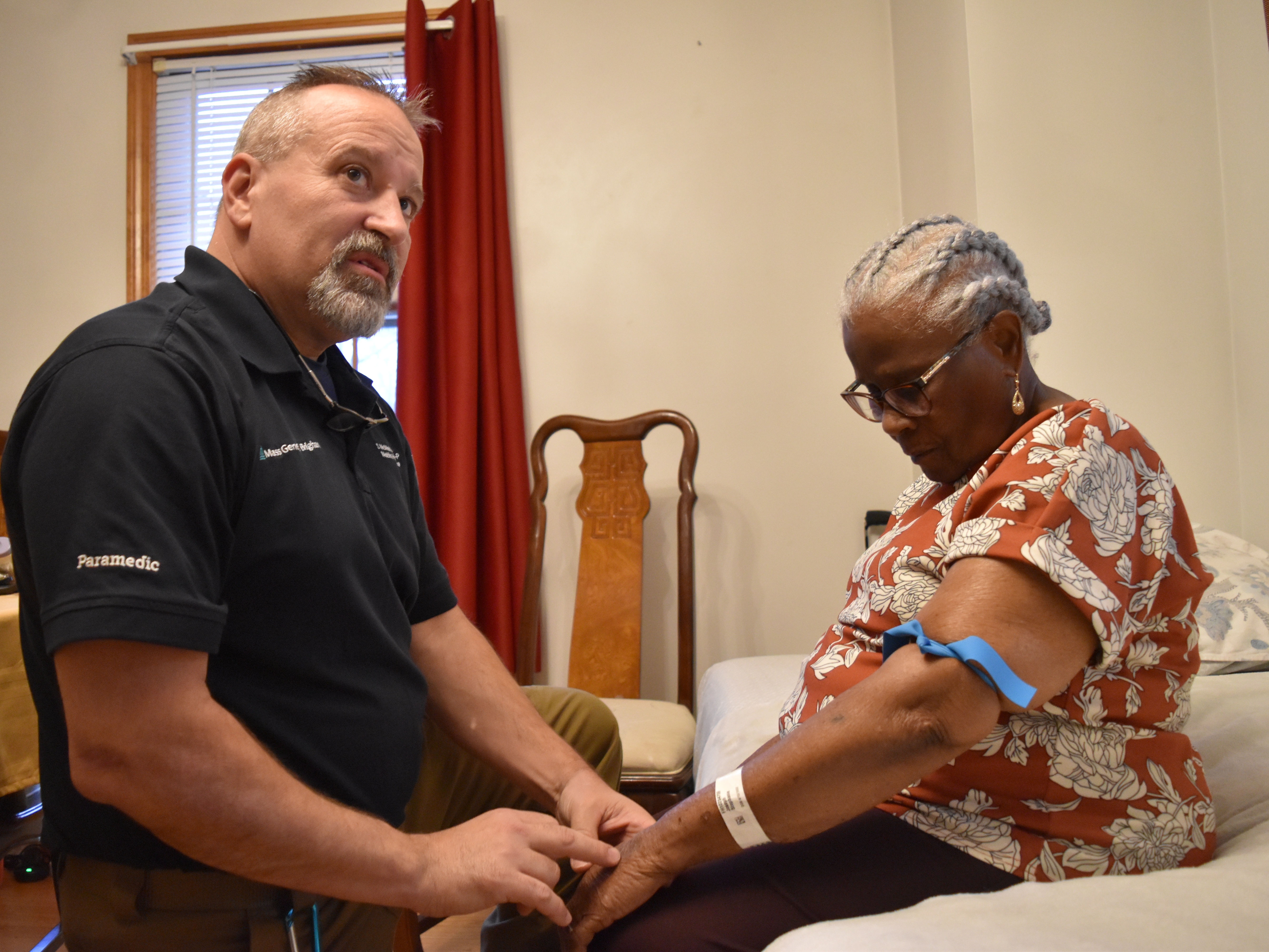 caption: Shane McMahon, a paramedic, checks on Stephanie Joseph, 91, who received care through Mass General Brigham's hospital-at-home program.