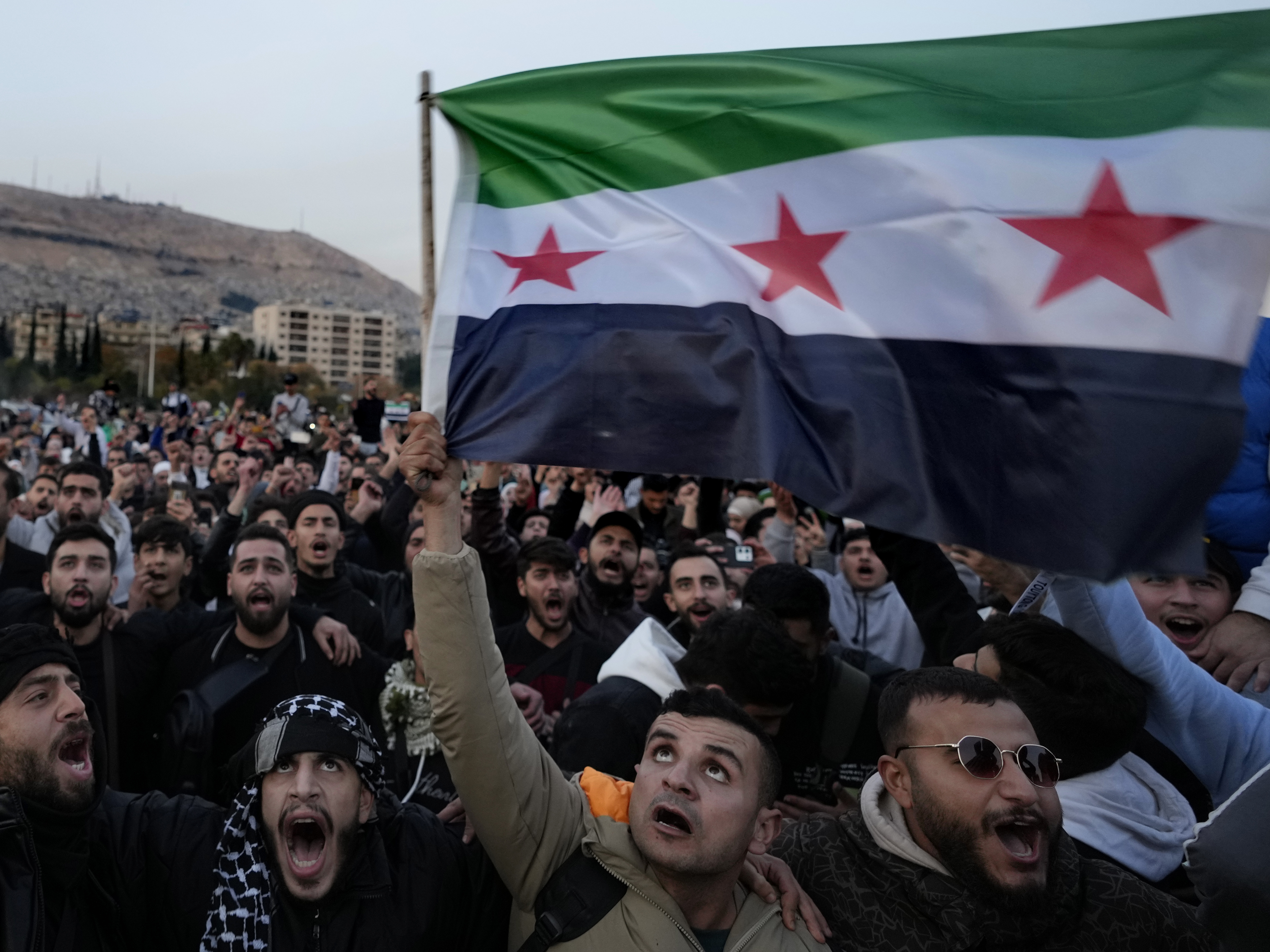 caption: Syrian citizens wave the revolutionary flag and shout slogans, as they celebrate during the second day of the take over of the city by the insurgents in Damascus on Monday.