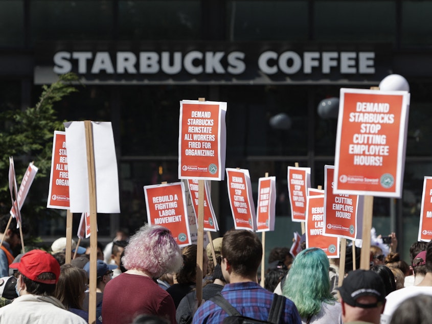 caption: A Starbucks coffee shop is seen in the background as people gather for a rally and march in Seattle on Saturday.