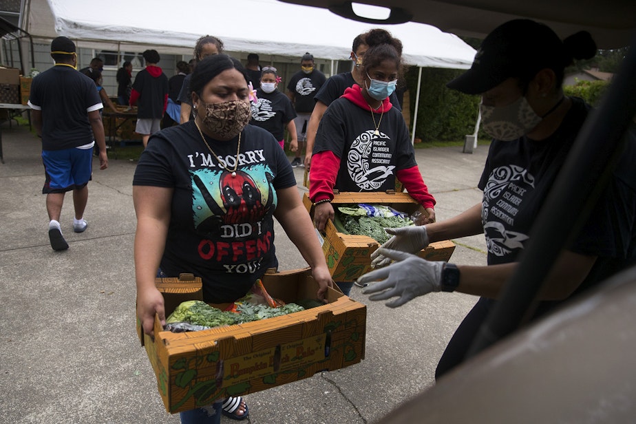 caption: Louise Chan Kau, left, loads boxes of fresh produce, meat and dairy into vehicles at a drive-thru free food distribution site led by the Pacific Islander Community Association of Washington on Thursday, July 10, 2020, along Military Road South in Kent. 