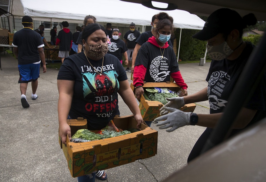 caption: Louise Chan Kau, left, loads boxes of fresh produce, meat and dairy into vehicles at a drive-thru free food distribution site led by the Pacific Islander Community Association of Washington on Thursday, July 10, 2020, along Military Road South in Kent. 