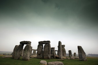 caption: Visitors and tourists walk around the ancient monument at Stonehenge in 2012 in Wiltshire, England.