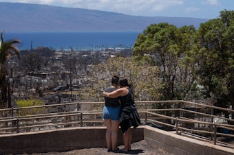 caption: Two women embrace and cry as they look out over a burned area in Lahaina, Hawaii in August 2023. A new survey finds most Americans expect the impacts of climate change to worsen in the next 30 years, as climate scientists warn.