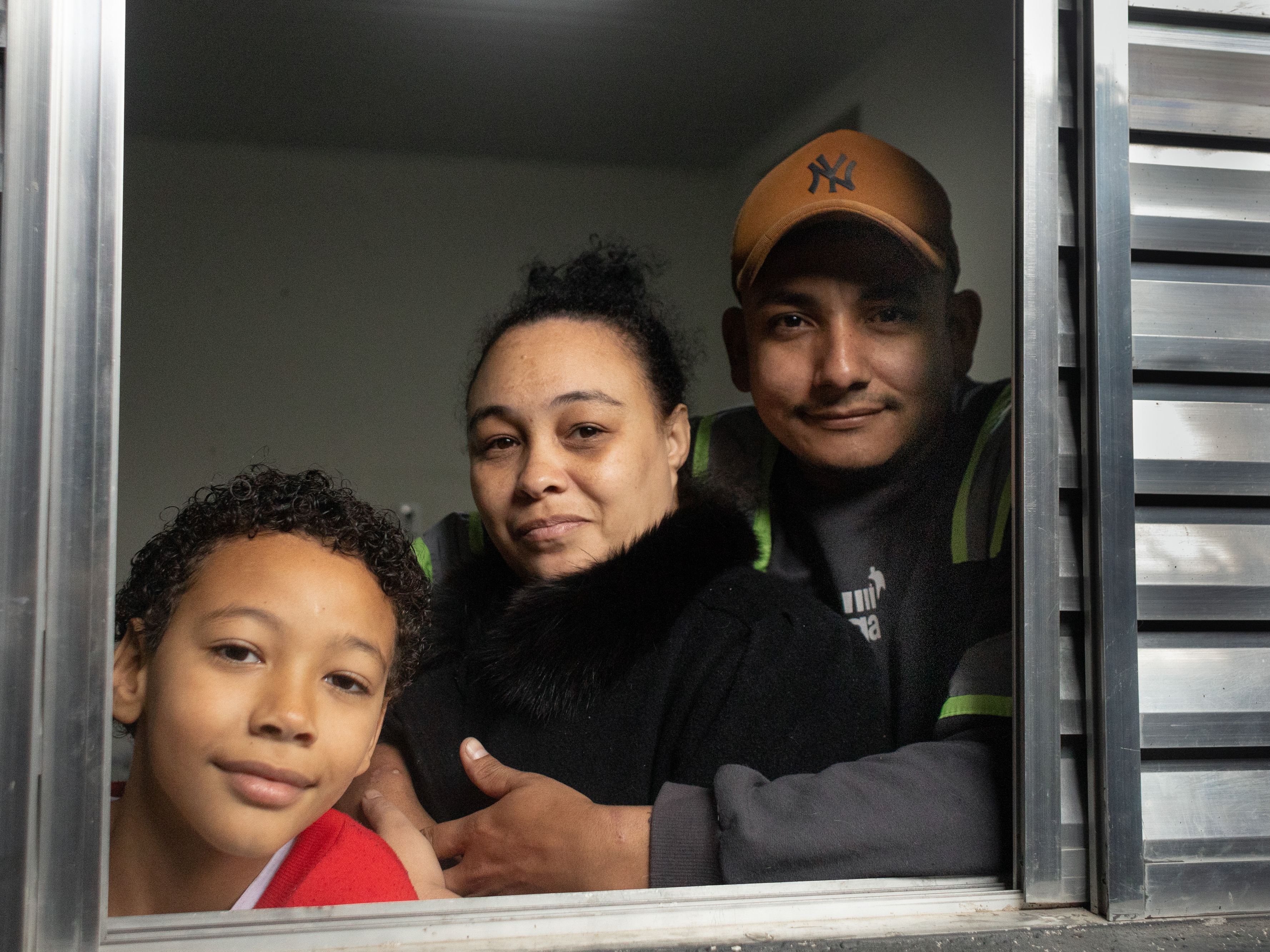 caption: Erica Lacerda de Souza, son Henrique and husband Bruce Lee de Souza, relax in their new home in Guaianazes, São Paulo. The family lost their home when the pandemic took away their livelihoods. They moved in about two months ago after being homeless, then getting a tiny transitional residence/