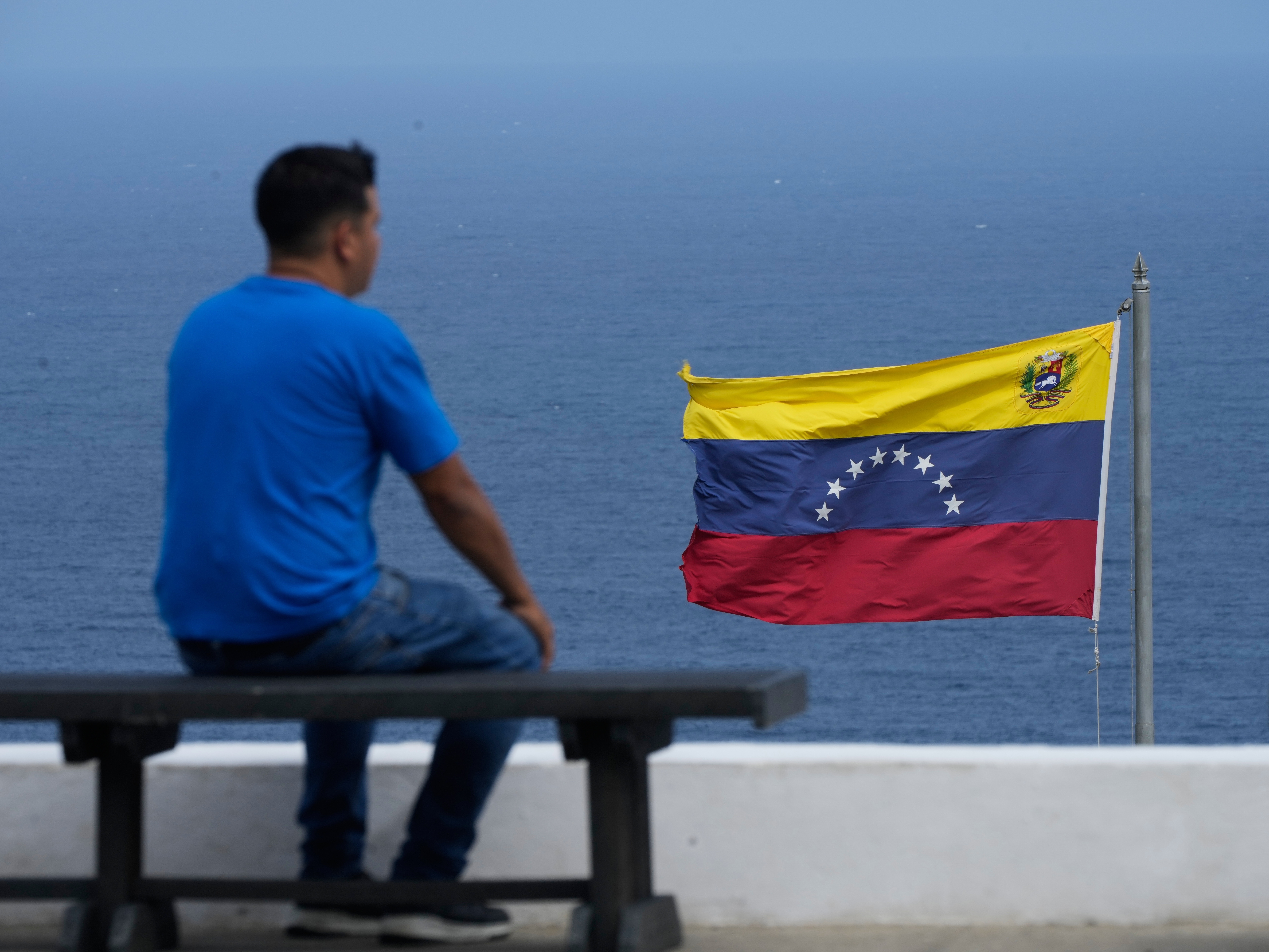 caption: A man looks out at the sea in the city of La Guaira, Venezuela, where the nation's flag flies, Wednesday, Dec. 17, 2025.