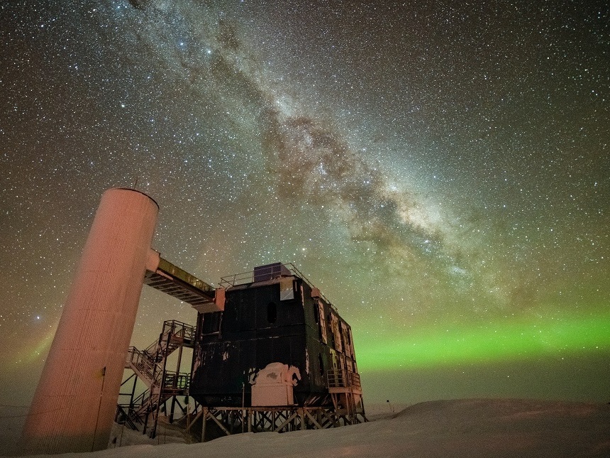caption: The IceCube Lab under a starry, night sky, with the Milky Way appearing over low auroras in the background.