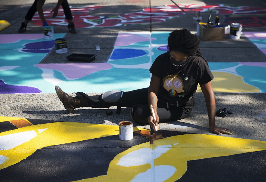 caption: Aramis O. Hamer paints the letter V in the Black Lives Matter street mural on Friday, October 2, 2020, on E. Pine Street in Seattle. 