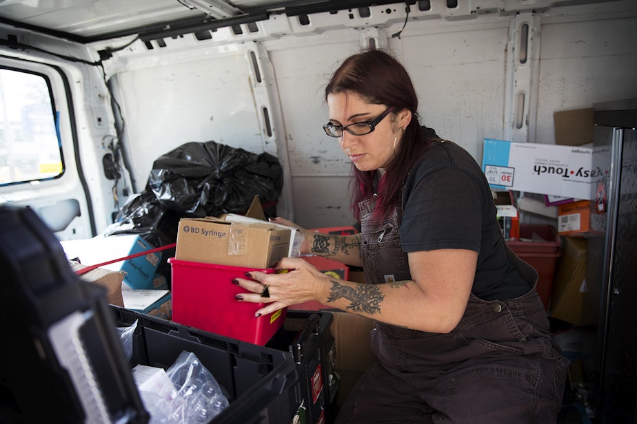 caption: Lisa Al-Hakim, Director of Operations at the People's Harm Reduction Alliance, moves a box of syringes before doing outreach along Aurora Avenue on Monday, May 6, 2019, in Seattle.