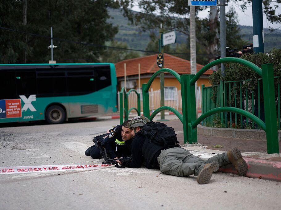 caption: Israeli security forces take cover during a siren alert while gathering at the site of a Hezbollah missile strike that targeted a bus in the northern Israeli border town of Kiryat Shmona on March 23, 2026.