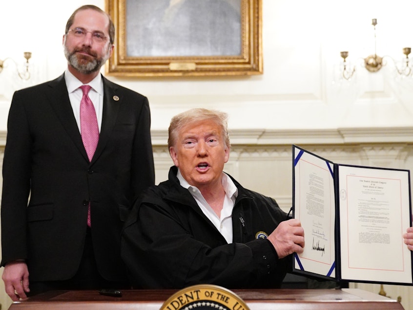 caption: President Trump holds up the $8 billion coronavirus emergency funding bill after signing it at the White House as Health Secretary Alex Azar looks on.