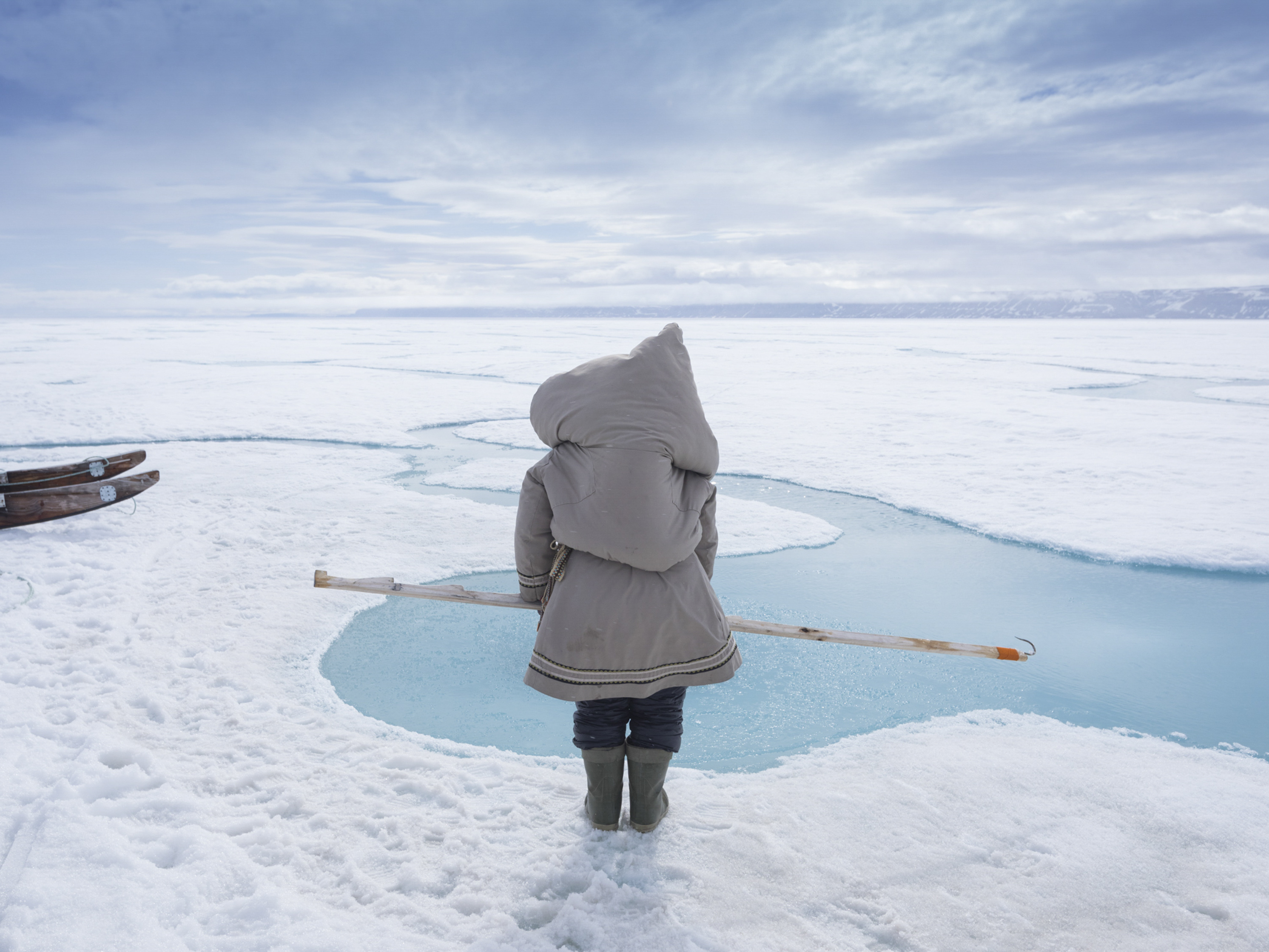 caption: Carrying her baby in a pouch on her back, Susan Enoogoo, age 39, hunts for ringed seal on the sea ice near Arctic Bay, Nunavut. Inuit mothers often carry their baby when hunting. If a seal surfaces, Enoogoo tries to snag it with the hook she's holding and drag it out of the water.