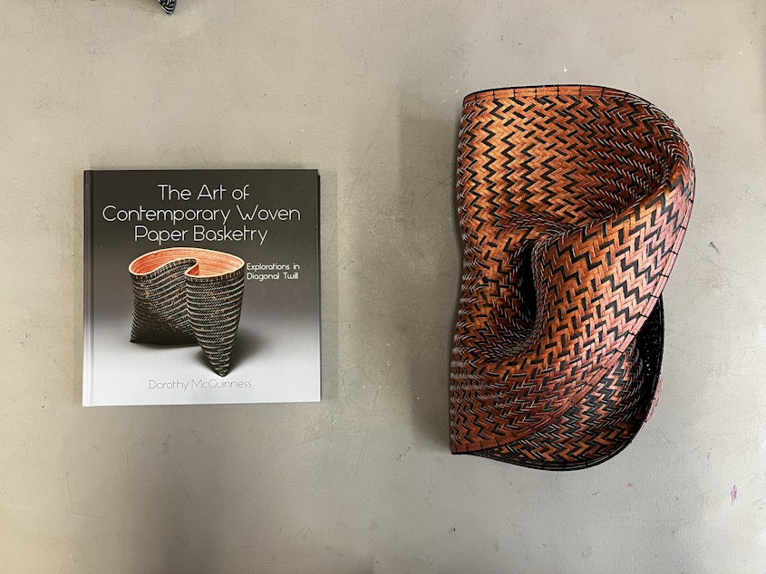 caption: The latest of Dorothy McGuinness' sculptural baskets, pictured alongside the book she authored on the subject. 