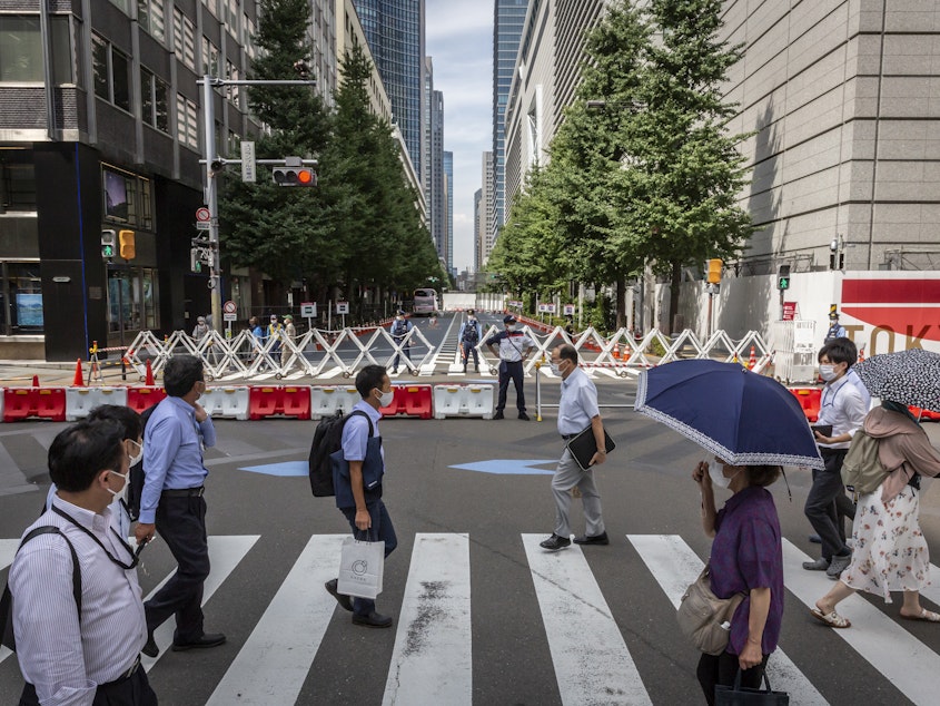 caption: Tokyo's government is reporting new daily coronavirus cases at a rate not seen in more than six months. Here, people cross a street next to the Tokyo International Forum.