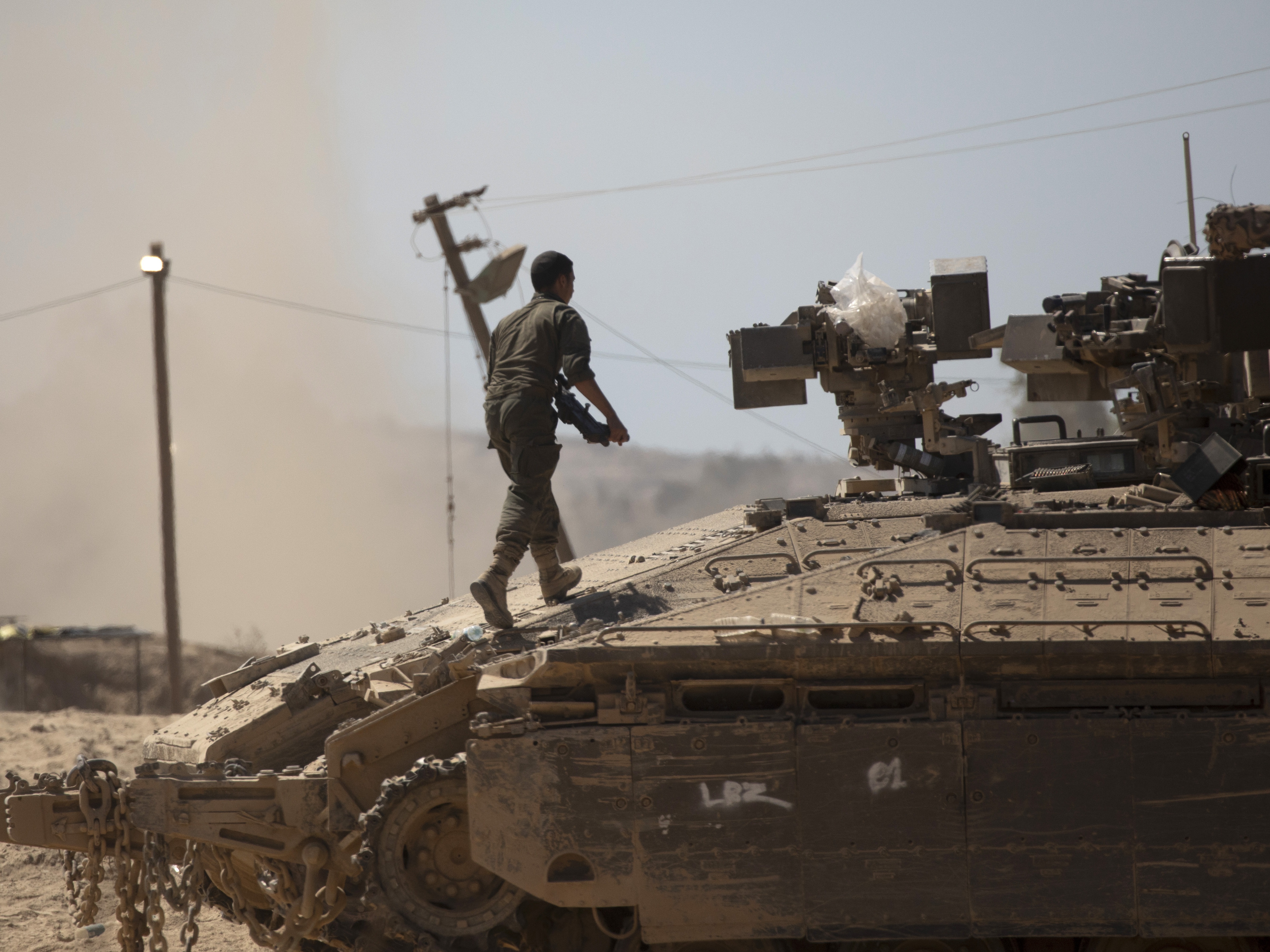 caption: An Israeli soldier walks on a tank near the border of the Gaza Strip in southern Israel on Aug. 21.