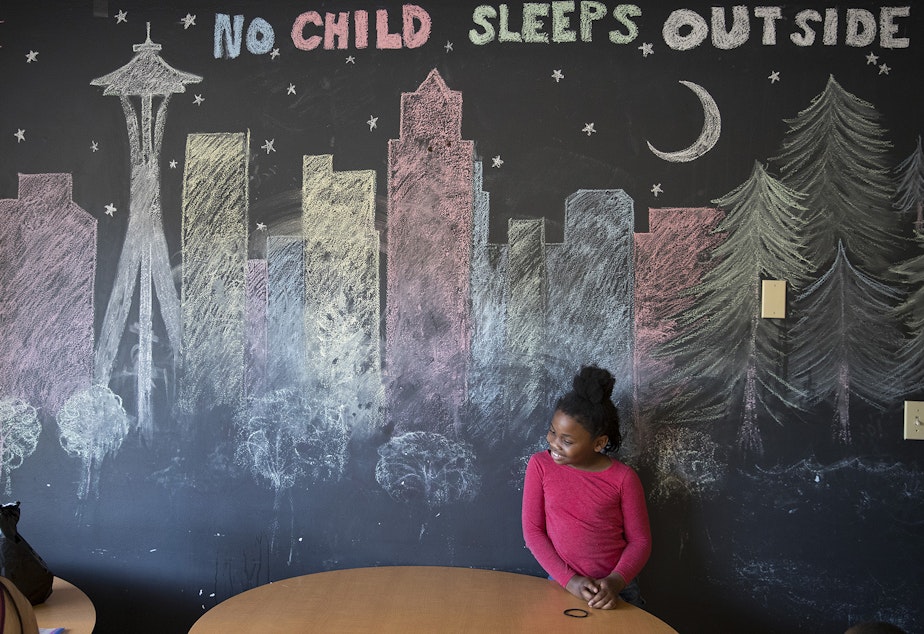 caption: Mariah Hicks, 7, in front of a chalk drawing depicting downtown Seattle in a common area at Mary's Place, on Monday, June 26, 2017, in Seattle.